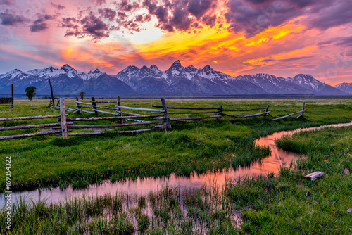 Photo Golden Fiery Sunset at Grand Teton - A colorful spring sunset at Teton Range, seen from an abandoned old ranch in Mormon Row historic district, in Grand Teton National Park, Wyoming, USA