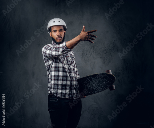 A man holds long board over grey background in a studio.