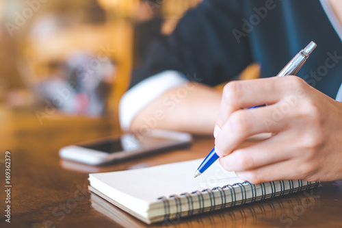 Business woman hand is on a notepad with a pen on a wooden desk in the office.