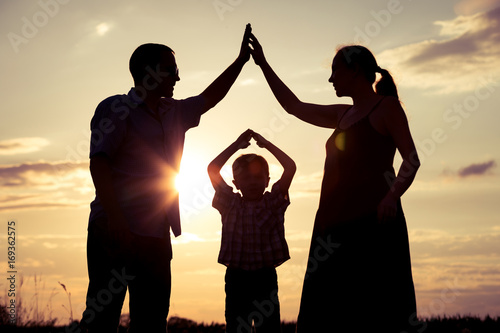 Happy family standing on the field at the sunset time.