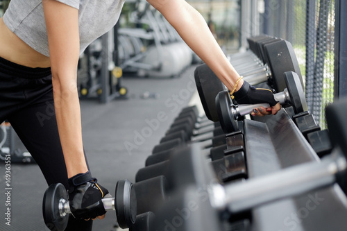 Fit woman wearing sports clothes weighing dumbbells in hands during workout in modern gym
