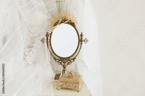 Old vintage oval mirror and beautiful white wedding dress and veil on chair. Copy space for mock up, montage or design layout