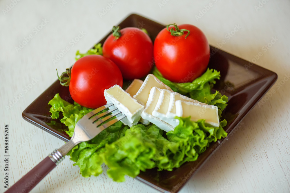 Tomatoes and cheese slices lie on a sheet of fresh salad in a plate.