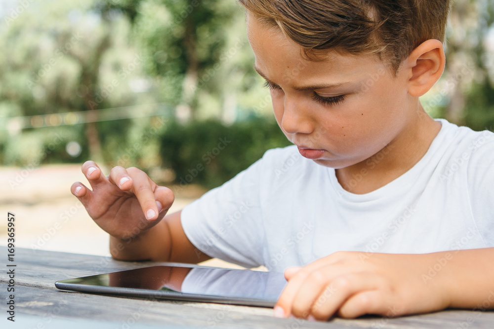 Kid tapping tablet in garden Kid tapping tablet in garden
