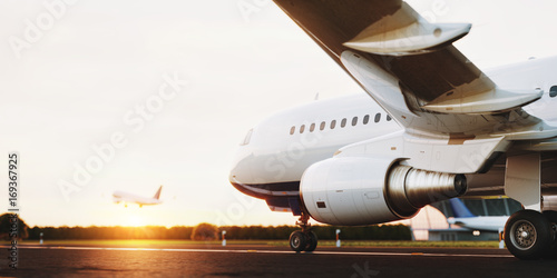 White commercial airplane standing on the airport runway at sunset. Passenger...