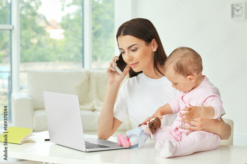 Young mother holding baby while working in home office Young mother holding baby while working in home office