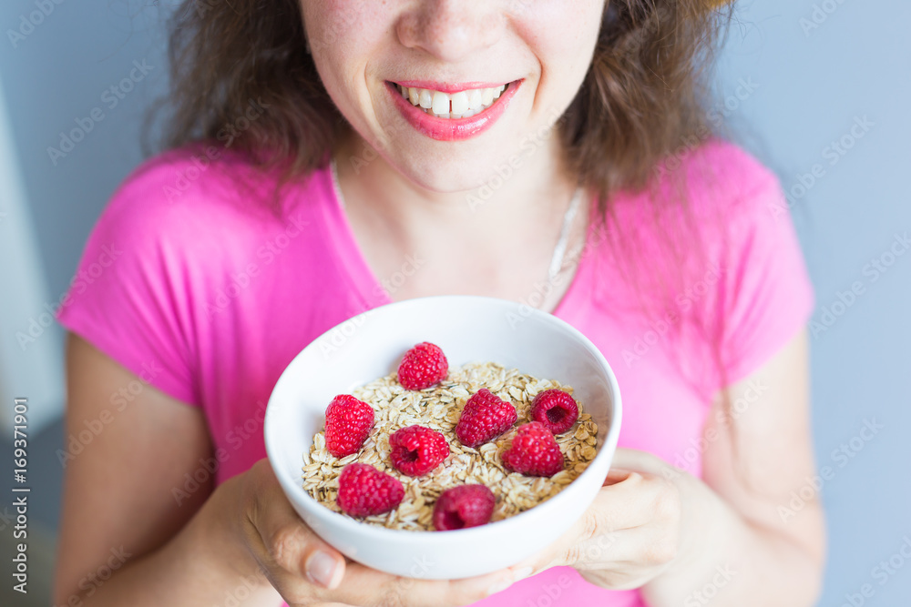 Woman's hands hold healthy and natural breakfast, oatmeal and raspberries in a bowl Woman's hands hold healthy and natural breakfast, oatmeal and raspberries in a bowl