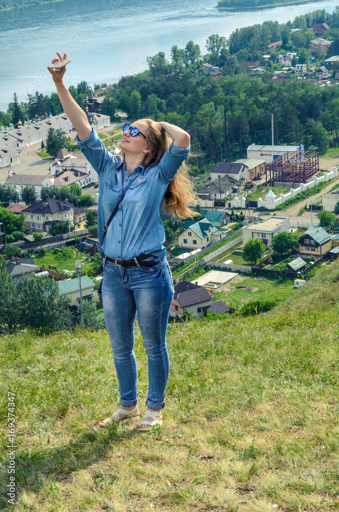 A young girl in blue clothes makes selfie on the background of a beautiful landscape