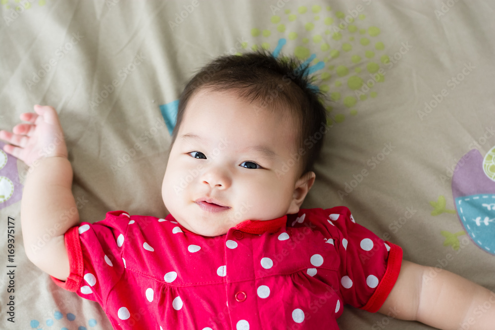 Portrait of adorable baby girl lying on back on the bed and looking in camera indoors Portrait of adorable baby girl lying on back on the bed and looking in camera indoors