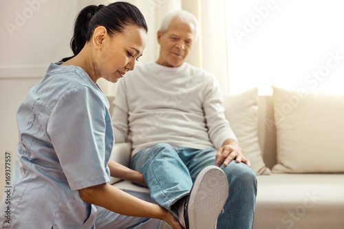 Delighted pleasant nurse looking at her patients leg