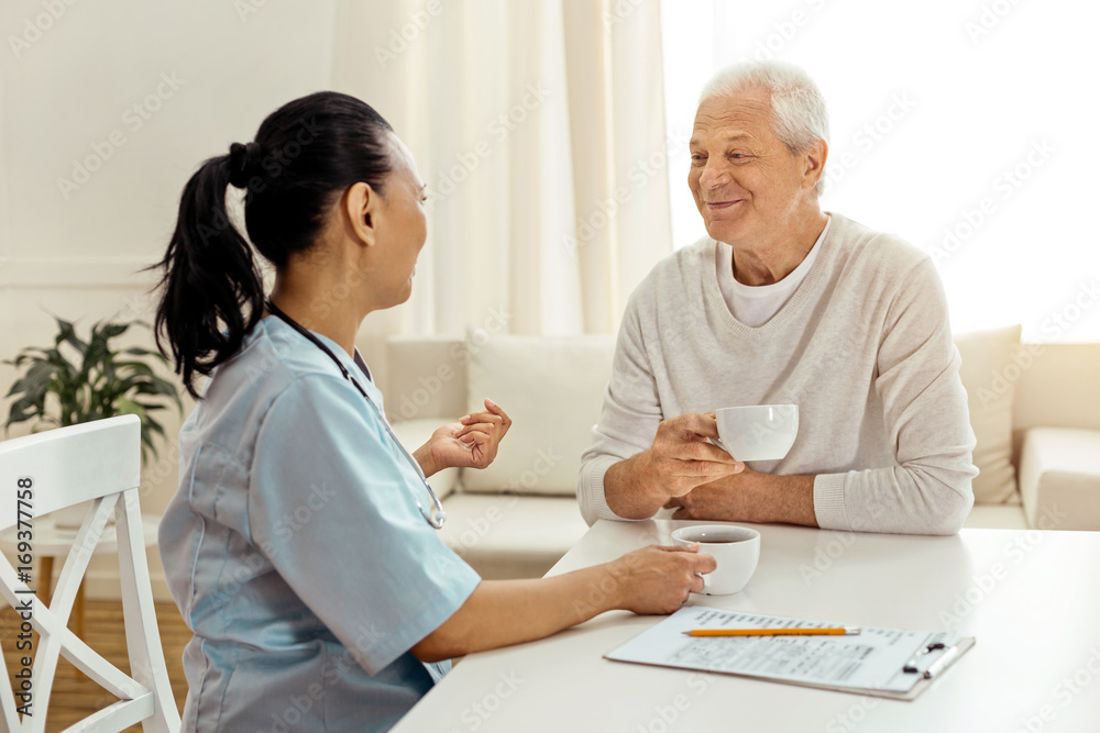 Positive nice caregiver and patient having tea
