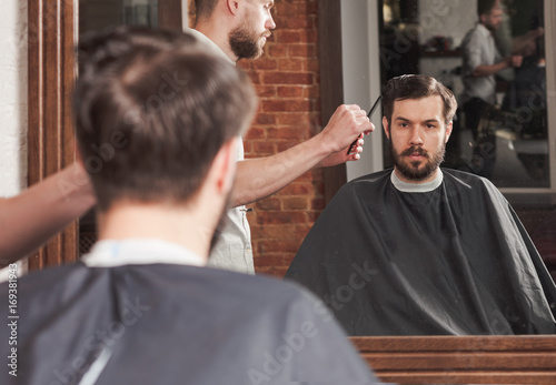 Young handsome barber making haircut of attractive man in barbershop