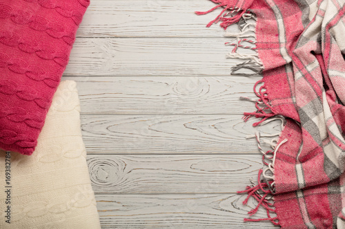 Knitted pillows and plaid on a light wooden background.