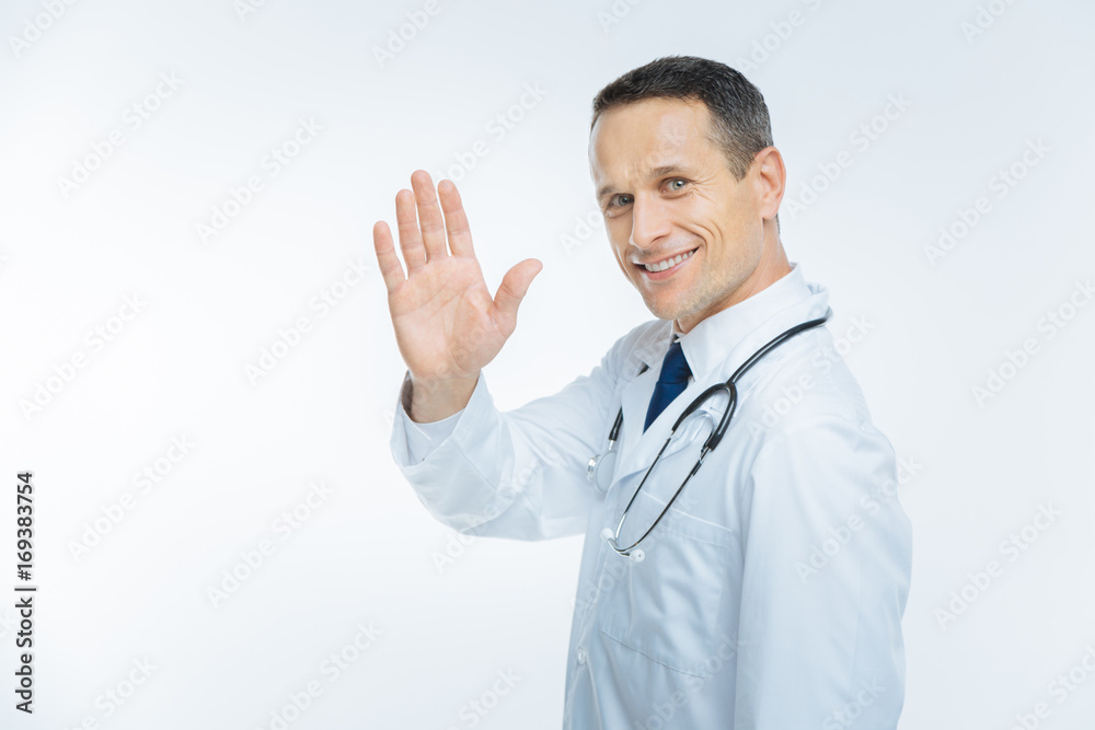 Positive minded mature doctor waving hello over background Positive minded mature doctor waving hello over background