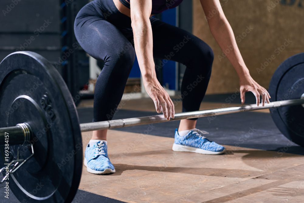 Low section portrait of unrecognizable young woman reaching out preparing to lift heavy barbell during weights workout in modern gym Low section portrait of unrecognizable young woman reaching out preparing to lift heavy barbell during weights workout in modern gym