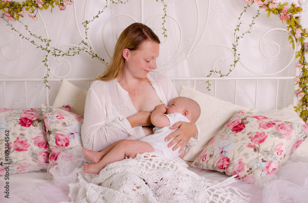 Breastfeeding baby. Young mother holding her newborn child. Mom nursing baby. Woman and new born boy in white bedroom.
