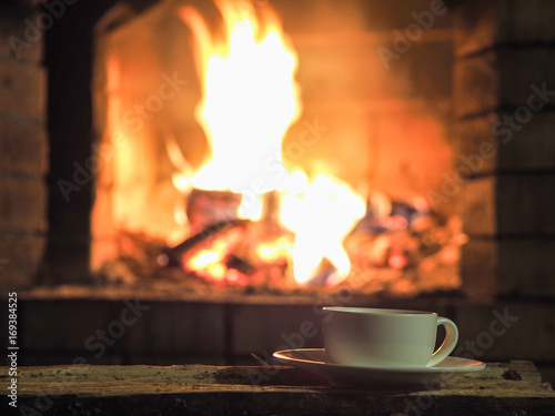 Cup of hot drink in front of warm fireplace. Holiday Christmas concept Cozy relaxed magical atmosphere in a chalet. Copy space.