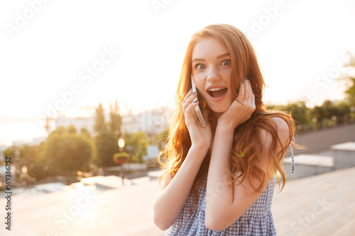 Amazed pretty redhead girl with long hair talking on phone