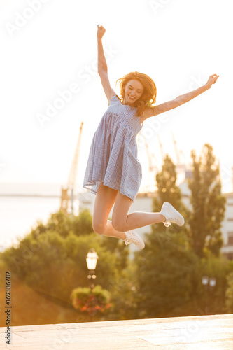 Happy young girl in dress jumping outdoors