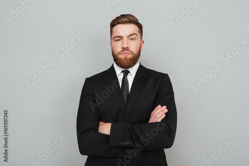 Canvas Print Confident young businessman in suit standing with arms folded