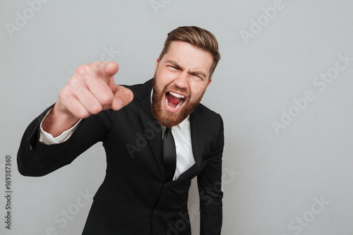 Angry businessman in suit shouting and pointing finger at camera