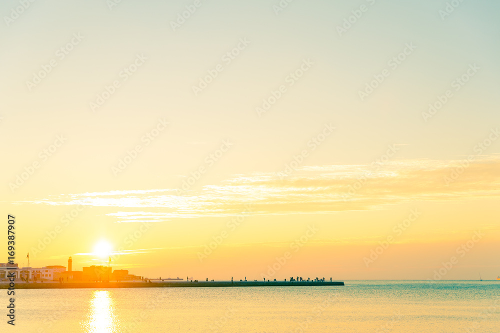 Naklejka premium people on rock pier with calm sea at sunset in italian town of trieste