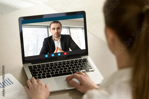 Businesswoman calling businessman online by video chat computer app, partners negotiating online on virtual meeting, employee reporting to boss running business remotely, close up rear view