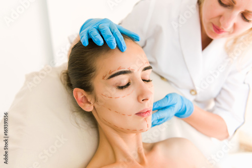 Doctor checking woman's skin before plastic surgery. Surgeon or beautician hands touching woman face.