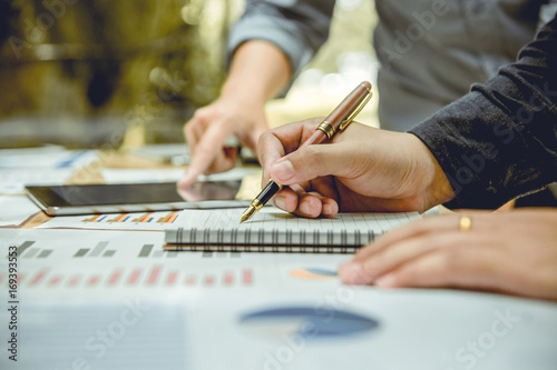 hand of businessman holding a pen and writing note book. There is his partner worker advising beside him.