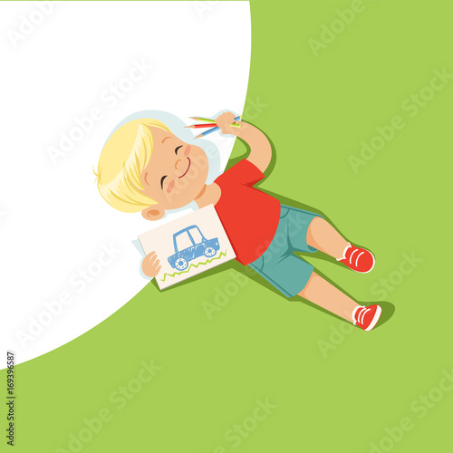 Little boy lying on his back and drawing with colorful pencils, top view of child on the floor