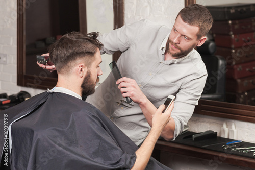 Young handsome barber making haircut of attractive man in barber