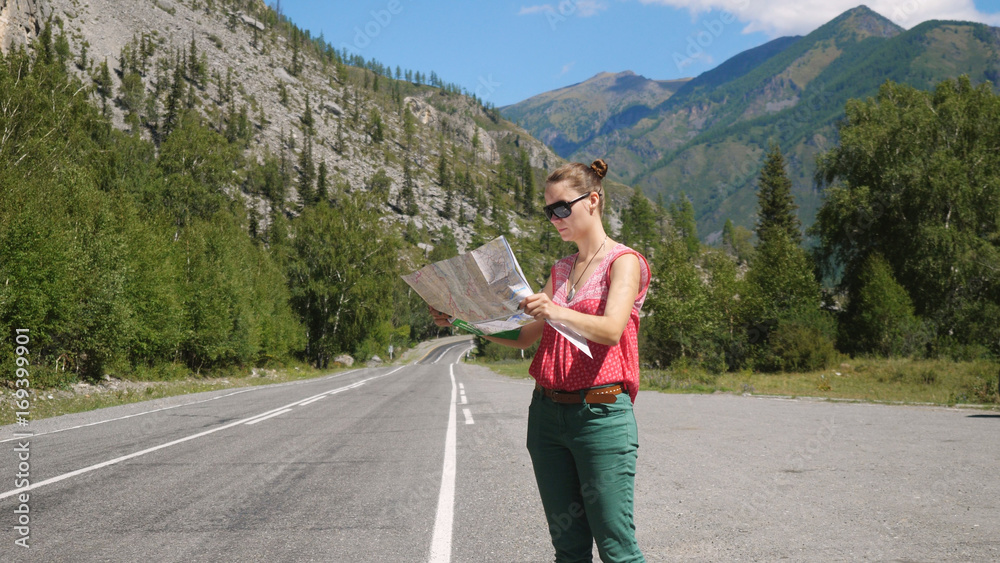 Tourist young woman wearing sunglasses chooses a travel destination on the map.