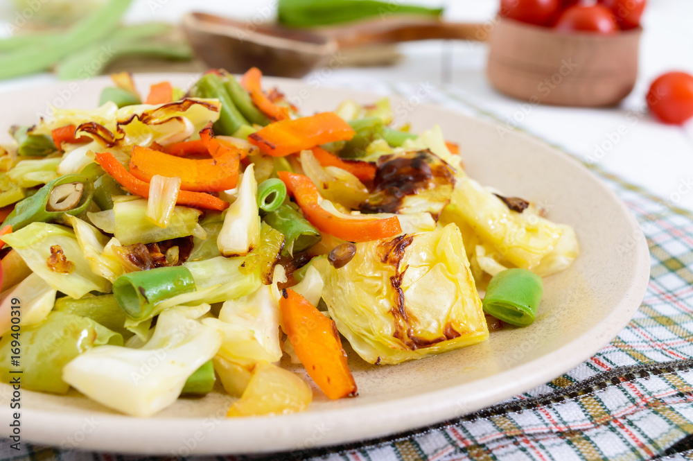 Vegetable stew - a mixture of baked cabbage, green beans, onions, carrots, cherry tomatoes, sweet pepper on a plate on a white wooden background. Vegan cuisine. Proper nutrition. Vegetable stew - a mixture of baked cabbage, green beans, onions, carrots, cherry tomatoes, sweet pepper on a plate on a white wooden background. Vegan cuisine. Proper nutrition.