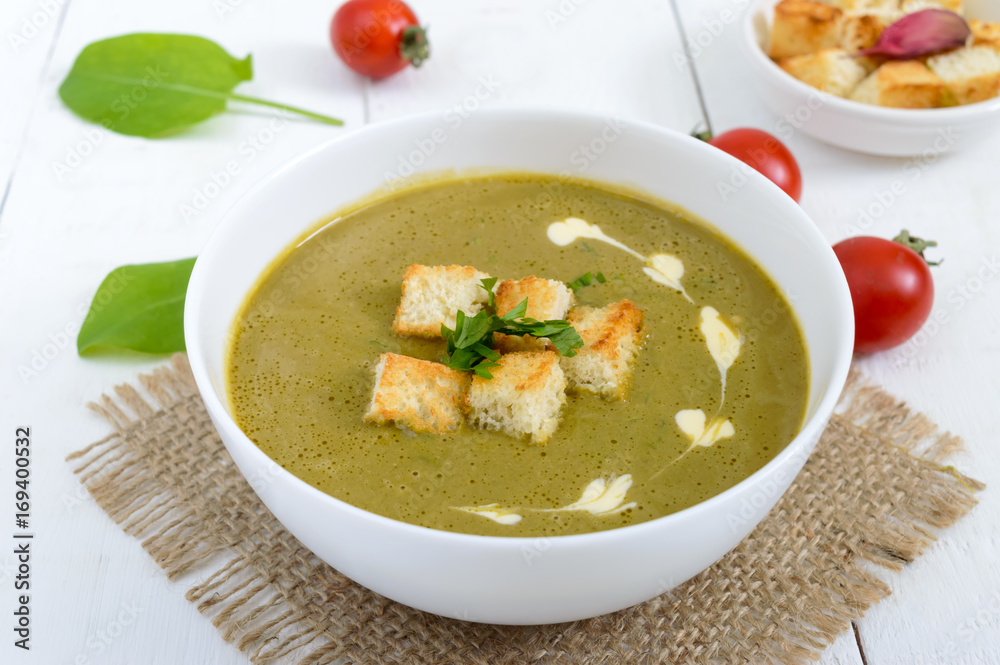 Light vegan spinach cream soup with crispy croutons in a bowl on a white background.