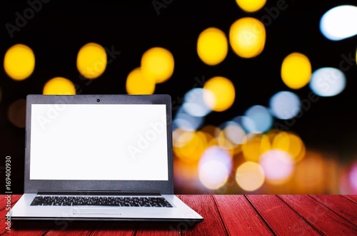 white blank screen laptop computer on wooden desk for presentation with blurred image of abstract night light bokeh on dark background, copy space, technology concept