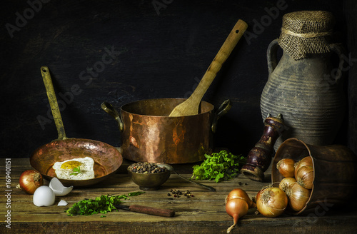 Classic still life with delicious fried egg placed with fresh basil,mixed pepper,onions and old pot on rustic wooden background