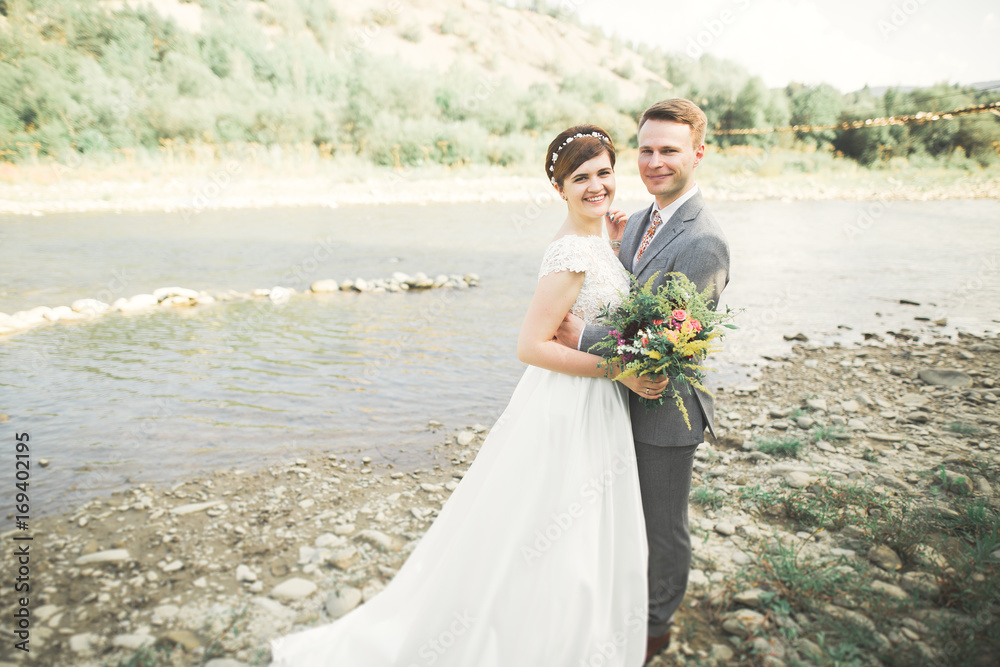 Bride and groom holding beautiful wedding bouquet. Posing near river