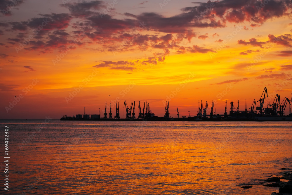 Beautiful landscape with fiery sunset sky and sea. Harbor of Berdyansk during sunrise. Cranes silhouettes against fiery, orange and red sky.