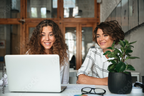 Two pretty smiling women working by the laptop