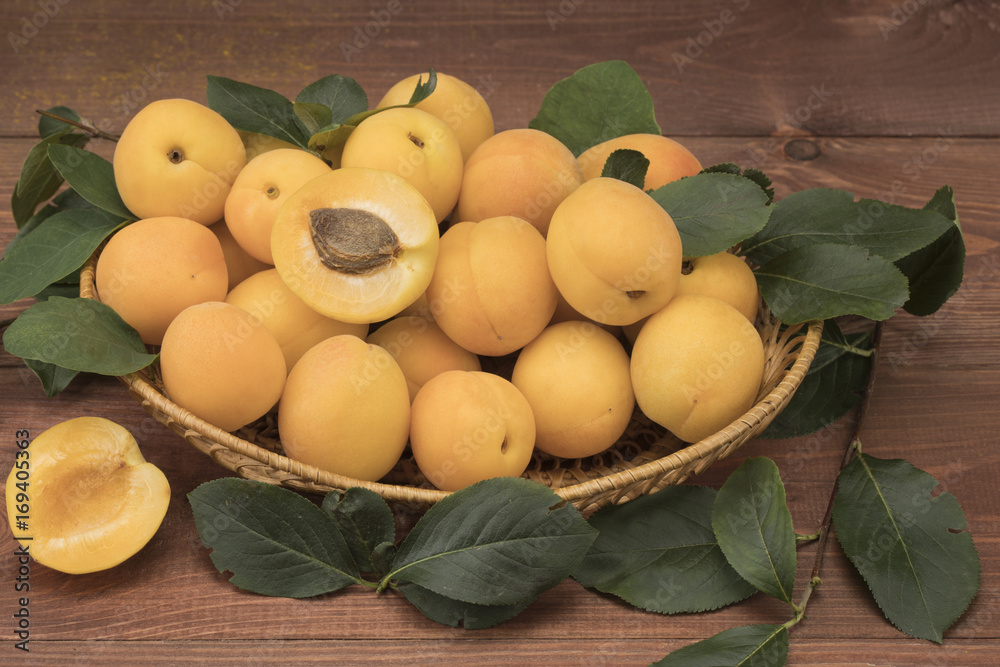 Fresh apricots on a wooden table with leaves and a basket