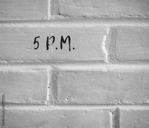 PHOTO OF 5 P.M. WRITTEN ON WHITE PLAIN BRICK WALL photo