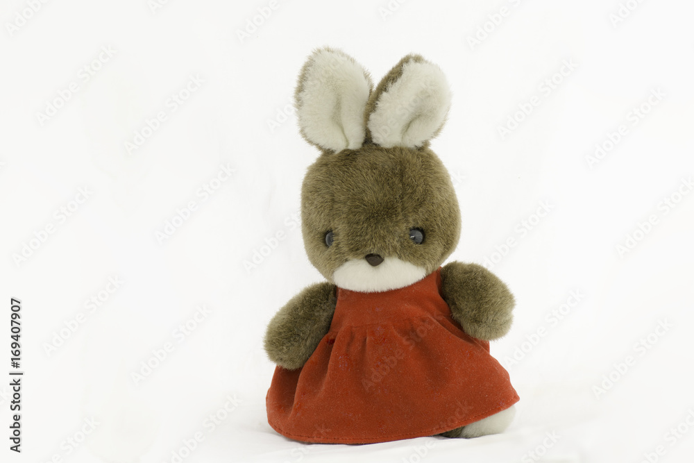 Fototapeta premium Rabbit doll wearing red dress standing on a white background.