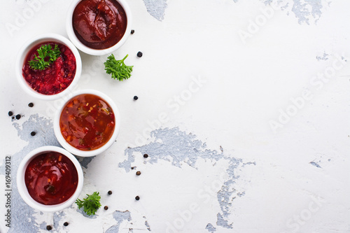 Bowls of various tomato sauces on white stone table. Top view. Copy space