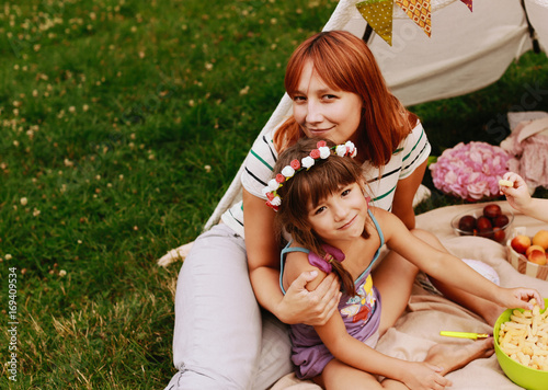 Mother hugs her little firl in flower wreath sitting on plaid outside photo