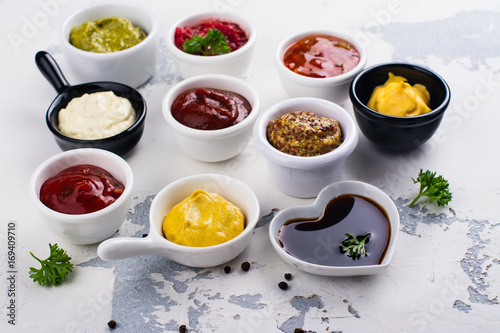 Various sauces and dips in porclean bowls on white stone background. Copy space