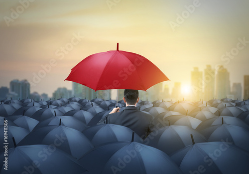 unique red umbrella among black umbrellas with city background photo