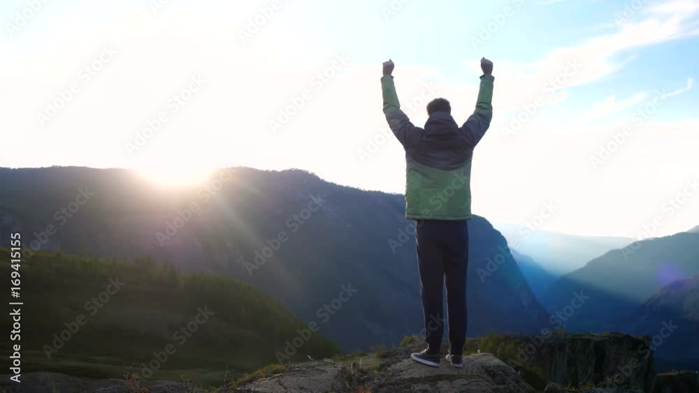 Success young caucasian man raising his hands high on top of the big mountain at beautiful golden sunset in slow motion with lens flare effects. 3840x2160 Success young caucasian man raising his hands high on top of the big mountain at beautiful golden sunset in slow motion with lens flare effects. 3840x2160