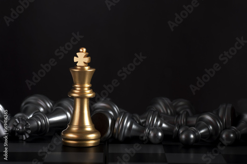 Gold king on a chess board surrounded by a number of fallen silver chess pieces with selective focus