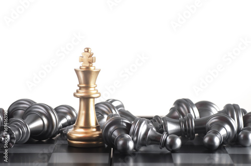Gold king on a chess board surrounded by a number of fallen silver chess pieces with selective focus