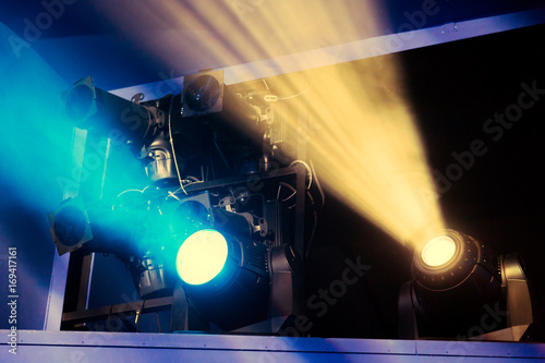 Lighting equipment on the stage of the theatre during the performance. The light rays from the spotlight through the smoke. Yellow and blue rays.